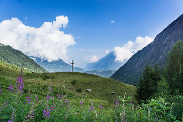 Wooden cross stands in a grassy meadow in the mountains of Switzerland