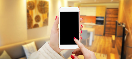 Women touching black screen of white smartphone. Colorful living room in background. Free space for text input.