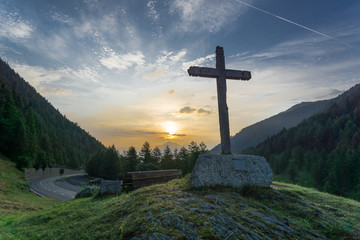 Wooden cross and colorful sunrise in a forested valley in the mountains of Switzerland