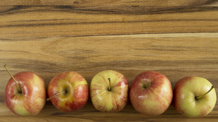 Apples lined up on bottom portion of wood cutting board