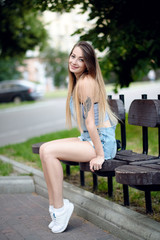Beautiful young girl sitting on a bench in the park in the summer and the rest