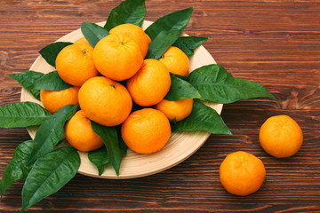 Ripe orange tangerines with green leaves in plate