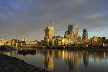 The view of the skyscrapers of City of London with its reflection on the Thames River in London, United Kingdom during a cloudy morning.