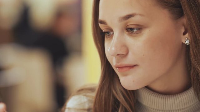 A young pretty girl reads and writes messages on the phone sitting in a cafe at the table. Close-up.