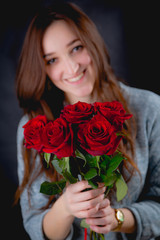 Pretty girl is holding a bouquet of red roses, dark background