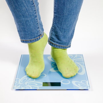 female feet in green socks standing on the blue scales