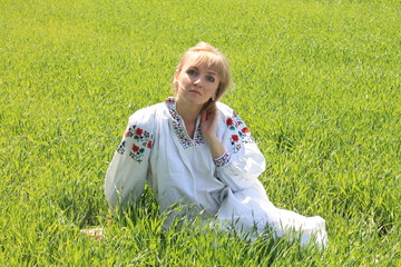Girl blonde in the spring of Ukrainian embroidery in the field between herbs and green grass