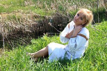 Girl blonde in the spring of Ukrainian embroidery in the field between herbs and green grass