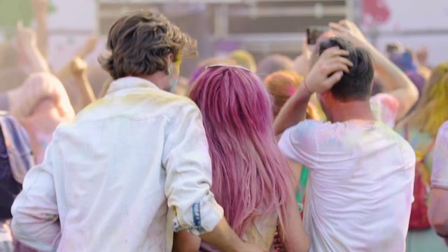 Excited people dancing, waving hands at traditional Holi color festival, slowmo