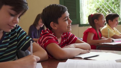 Young people and education. Group of hispanic students in class at school during lesson. Happy boy smiling and sitting at desk - Powered by Adobe