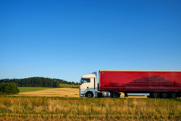 White truck with a red trailer riding on a road horizon along the agricultural fields under blue skies