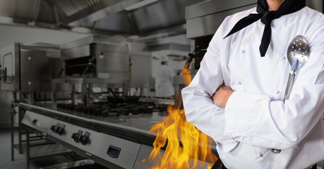 Mid section of chef standing with arms crossed in kitchen