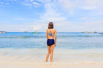 Fototapeta na wymiar Asian woman in swimsuit standing poses on beach with happy and beautiful blue sky above the sea, Similan Island, Similan National Park, Phang Nga, Thailand