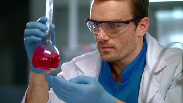 Scientist doing laboratory research. Closeup of scientist looking at liquid in laboratory flask. Scientist face at research lab. Scientist research liquid in lab flask at research laboratory