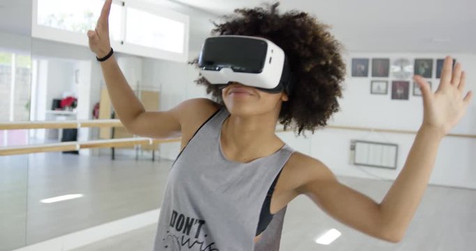 African american girl using VR glasses while dancing in modern mirrored studio.