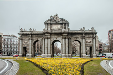 Obraz premium Puerta de Alcala view surrounded by yellow flowers. Puerta de Alcala is one of the most iconic landmarks in the city of Madrid, Spain.