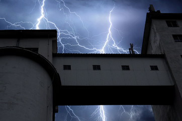 Lightning and thunder on stormy summer night over factory building