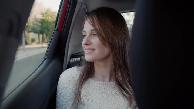 Beautiful woman smiles looking outside through the window in the backseat of a car.