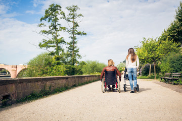 Young Parents In Wheelchair With Baby Stroller In The Park