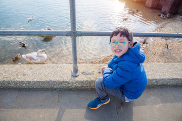 Young asian boy watching ducks and swans in the river