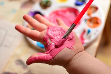 Child painting her hand with pink paint and background with palette of colorful paint