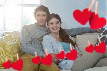 Composite image of red heart and couple embracing on sofa