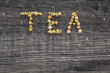 Word tea. Dried chamomile herbal tea on the wooden table as background. Healthy drink.