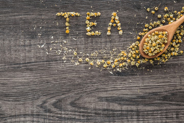 Word tea. Dried chamomile herbal tea on the wooden table as background. Healthy drink.