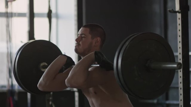 Handheld tracking of determined shirtless sportsman doing front squats and then dropping barbell 