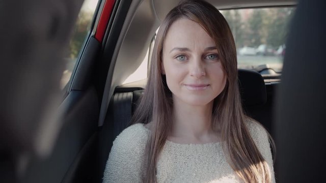 Beautiful woman smiles looking at camera in the backseat of a car. The car is stopped.