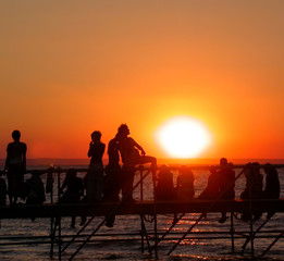 Naklejka na ściany i meble Group of young people on the ocean beach watching the sunset during beach party