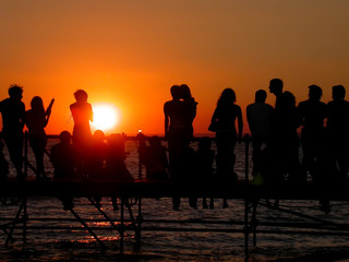 Fototapeta na wymiar Group of young people on the ocean beach watching the sunset during beach party