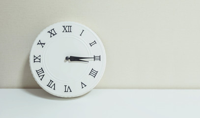Closeup white clock for decorate show a quarter past three or 3:15 p.m. on white wood desk and cream wallpaper textured background with copy space