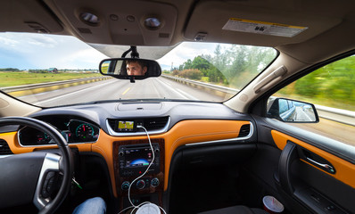View from luxury car inside with part of interior gps screen with driver man face in mirror. Car moveing on American hihtway.