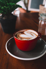 A red cup of coffee with white foam on the wooden table