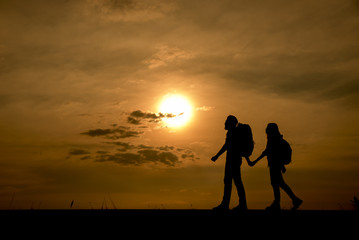 Fototapeta na wymiar Silhouette of two backpackers (man and woman) who were traveling.The background image is a sunset in Thailand.Man and woman are walking hand in hand.