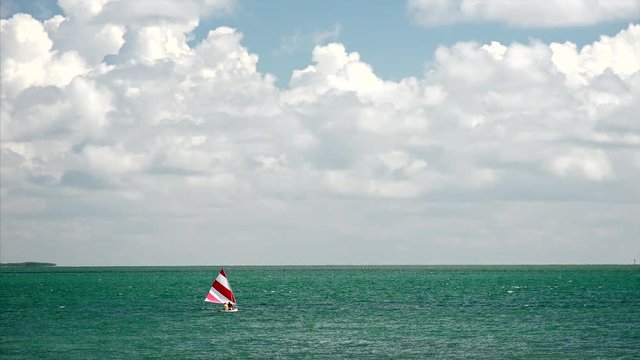 Dreamy sailboat with red and white striped sail in the tropical ocean of the Florida Keys