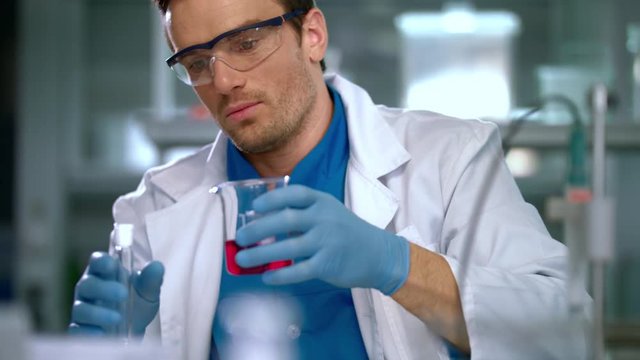 Scientist man carrying out scientific research in a lab. Young researcher working with liquid in chemical lab. Male scientist pouring liquid glass flask. Lab worker carrying out scientific research
