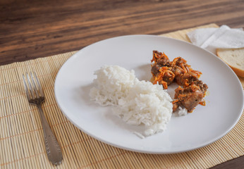 Scene with snow white ceramic dish of rice and roast meat, stew, meats with vegetables on a bamboo napkin on a wooden table from the old boards. Slices of white bread on the white paper napkins
