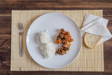 Scene with snow white ceramic dish of rice and roast meat, stew, meats with vegetables on a bamboo napkin on a wooden table from the old boards. Slices of white bread on the white paper napkins