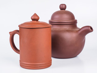 Picture of the brown infuser teapot near light brown tea cup. Infuser teapot and tea cup on white background. Handmade earthenware. Side view.