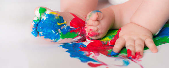 Baby child draws with colored paints hands, dirty feet.  Selective focus