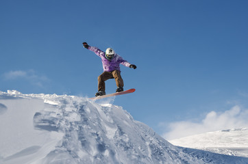Naklejka na ściany i meble Stylish snowboarder with helmet and mask jumps from high snow slope
