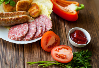 Grilled sausages and meat with vegetables and sauce on the table. On the wooden background, banner for cafe