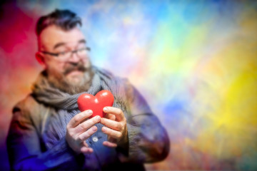 Adult bearded man in a blue jacket and scarf with disgust holding red heart  on a multicolor background