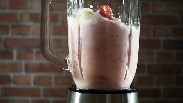 Blender with a banana strawberry milk smoothie on the kitchen, slow motion