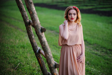 Yong elegance blonde girl at rose dress on the garden background