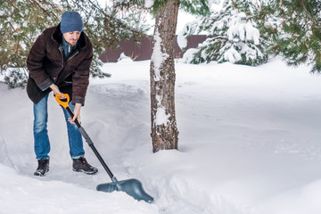 Man in winter clothes cleans snow shovel on courtyard