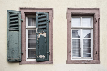 Two old windows, one of them with wooden shutters and flaking off paint and another without shutters