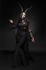 Young woman in black fantasy costume with big horns on dark background